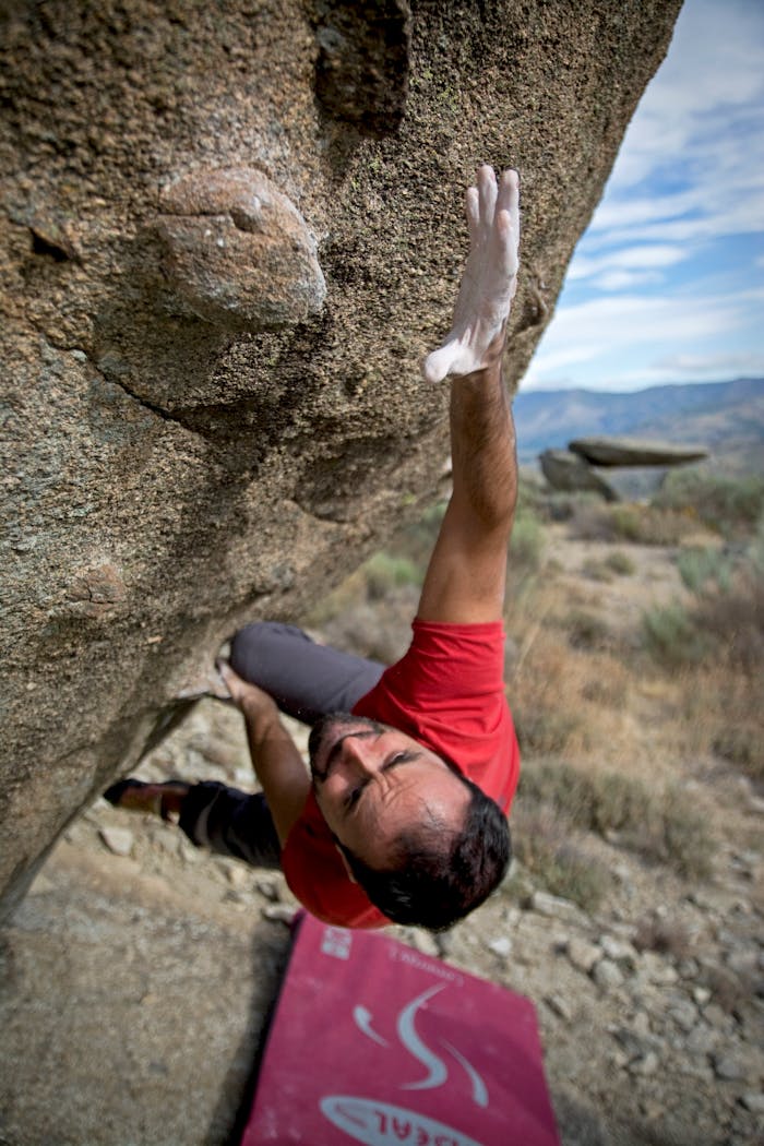 services-04 Man in red shirt bouldering on a steep rock face, showcasing strength and determination.