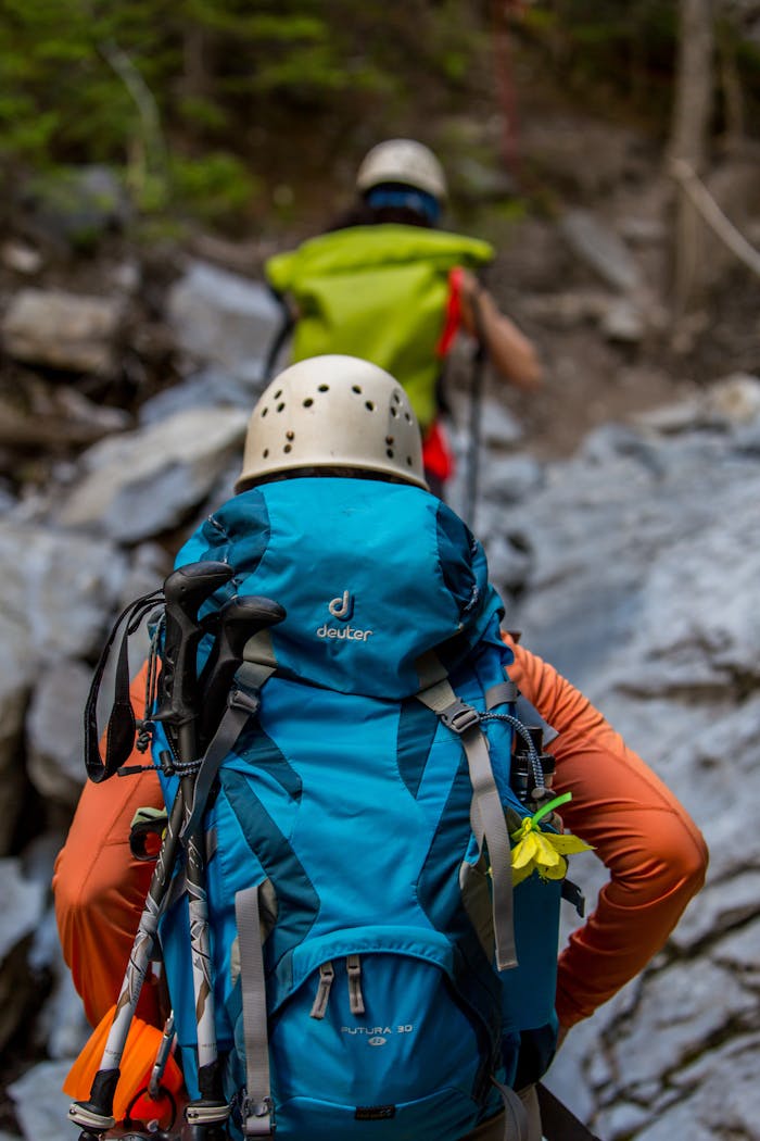 Two hikers with backpacks and helmets navigating a rocky trail in the forest.